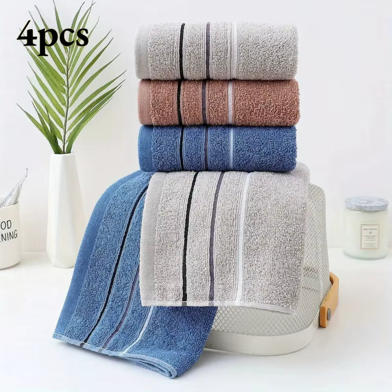 Stack of folded towels in grey, brown, and blue colors with a plant and candle on a white surface.