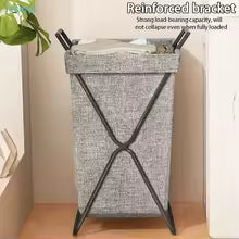 Gray laundry basket with X-shaped handle on a wooden floor, reinforced bracket visible.